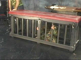 Woman in camo is locked in a petite cage whilst old boy-friend looks on